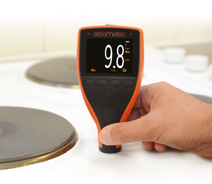 An individual holding the Elcometer 415 Paint & Powder Coating Thickness Gauge against the top of a stove between the hobs to measure the painting thickness