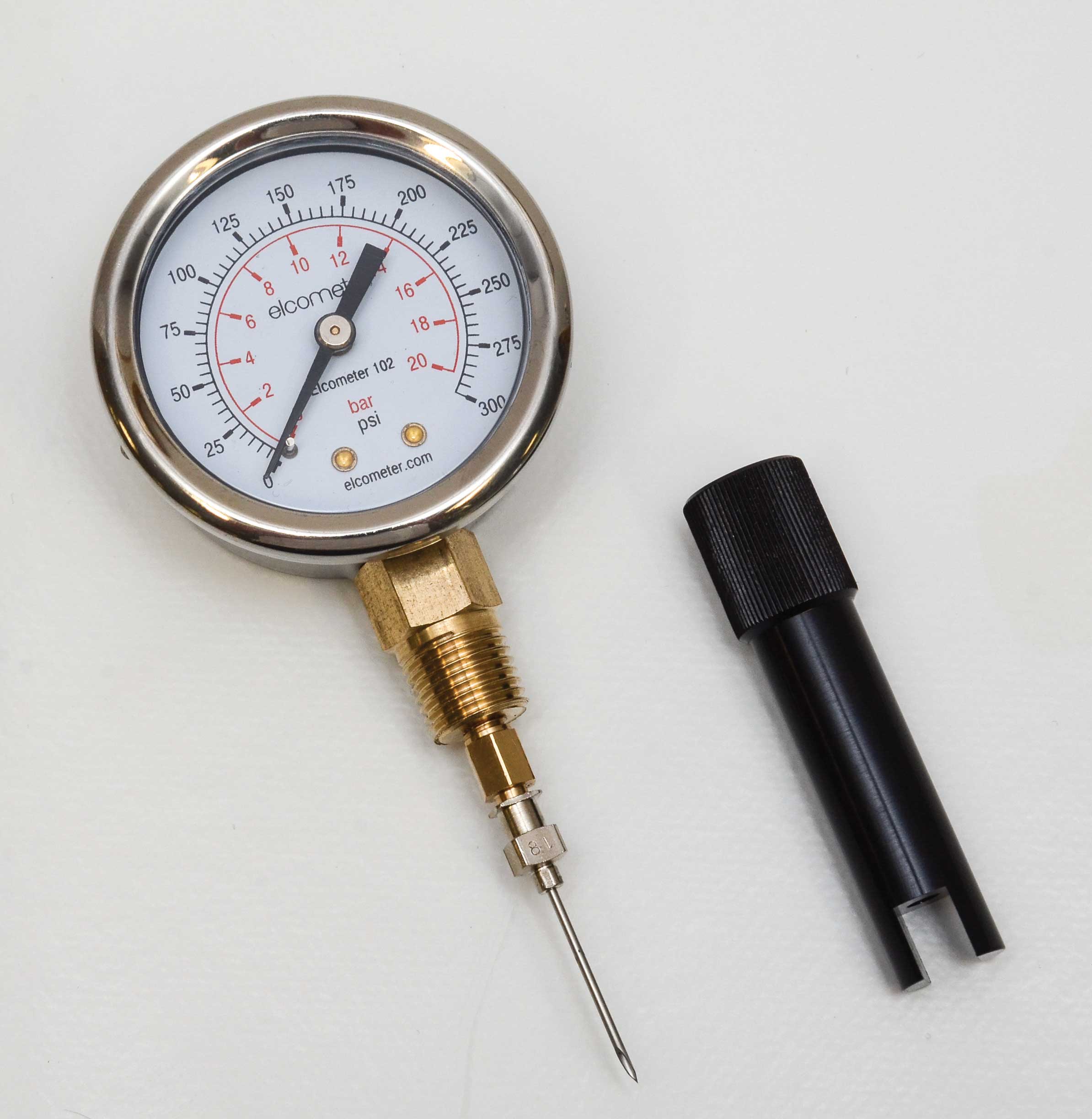 A golden pressure gauge that has a circular meter face which ranges from 0 to 300. The black arrow is currently pointing towards 0 psi and 0 bar. The meter is lay on its back with a black nozzle lay to the right of it.