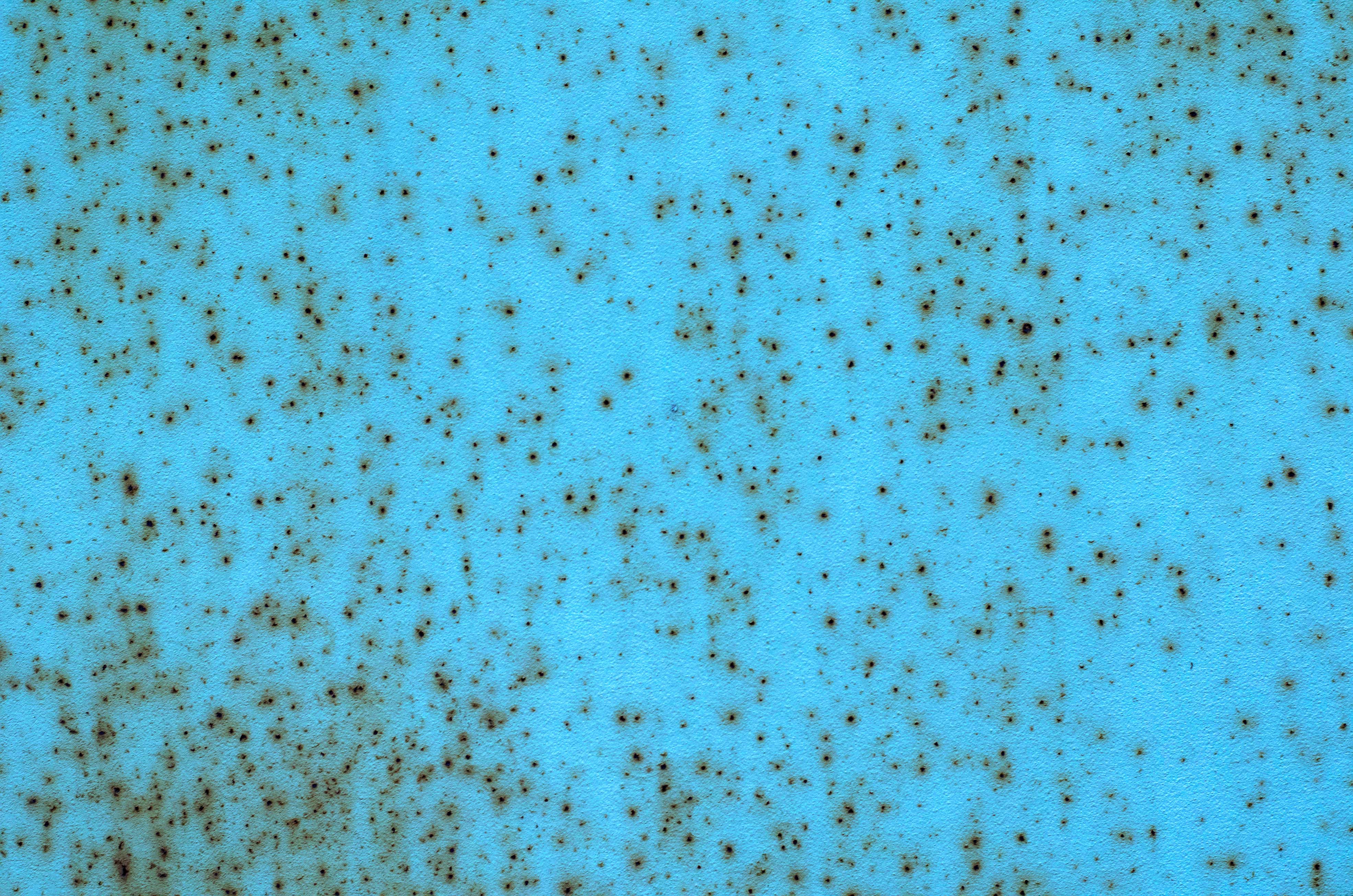A bright blue coated steel surface that is covered in small, dark rust spots