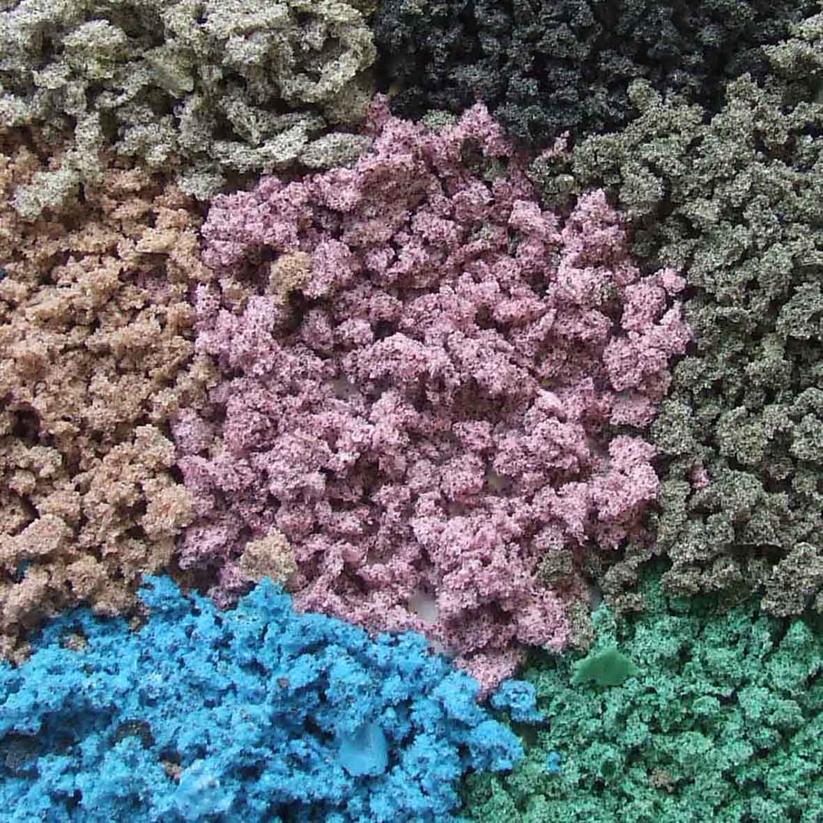 Seven piles of tiny stones that resemble sand. Pink is in the middle and around the outside is beige, light grey, black, dark grey, green and blue. They're all uneven surfaces.